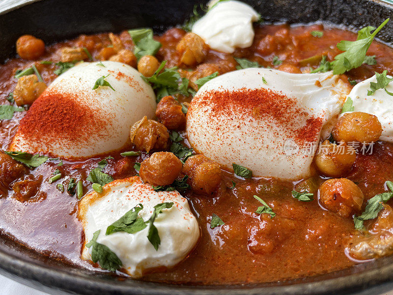 一锅地中海健康早餐的全画幅图片:shakshouka / shakshuka / chakchouka，鹰嘴豆，鸡蛋在番茄，辣椒，洋葱，橄榄油和大蒜的酱汁中水煮，顶部有香菜，高架视图，重点在前景